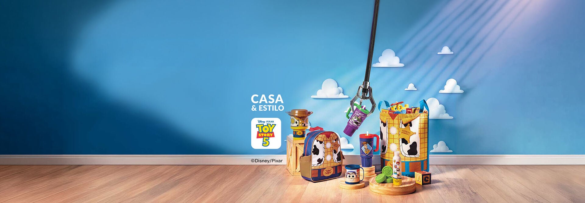 Cenário azul com nuvens e produtos de Toy Story 5 no chão de madeira: mochila, copos, caneca, shampoo, sabonetes e organizador de brinquedos. Uma garra mecânica suspende um copo no centro. 