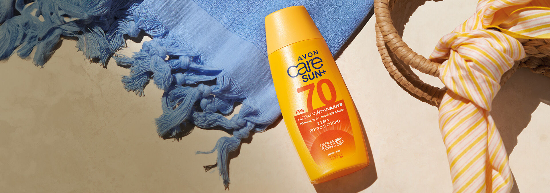 Banner com fundo bege. Elementos como toalha azul, cesta de palha e tecido listrado. Produto: protetor solar Avon Care Sun+ FPS 70. Texto: "Proteção solar para todos os corpos e peles."