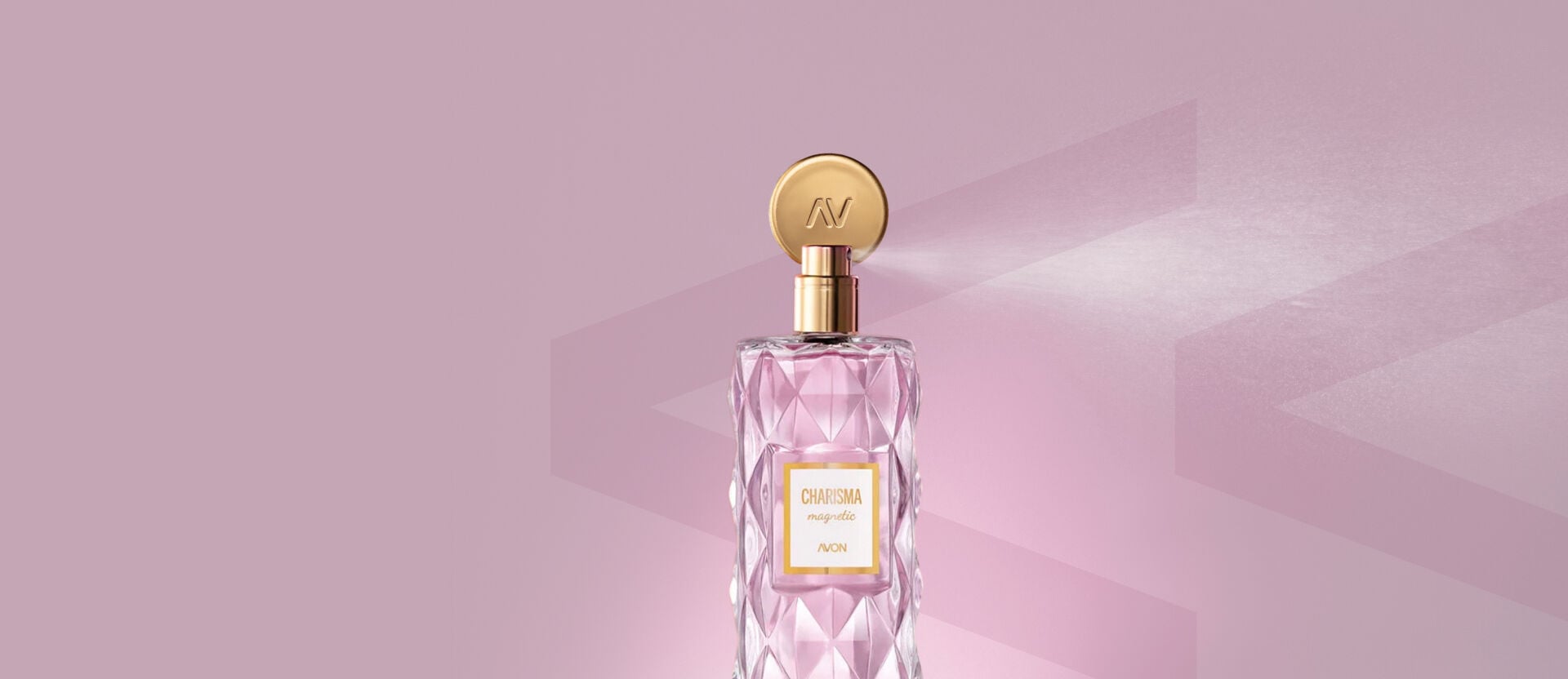 Deo Parfum Charisma Magnetic Avon em frasco transparente facetado, com líquido rosa e tampa dourada. A válvula spray dourada borrifa a fragrância, em um fundo rosa-claro.