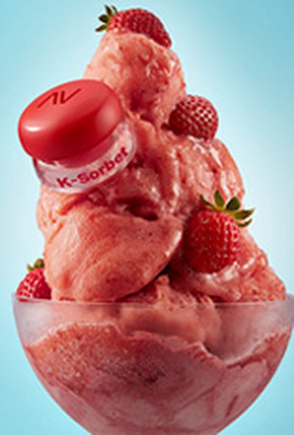 Embalagem Avon Balm Multifuncional K-Sorbet sobre sorvete com pedaços de morangos em taça translúcida. Fundo azul-claro.