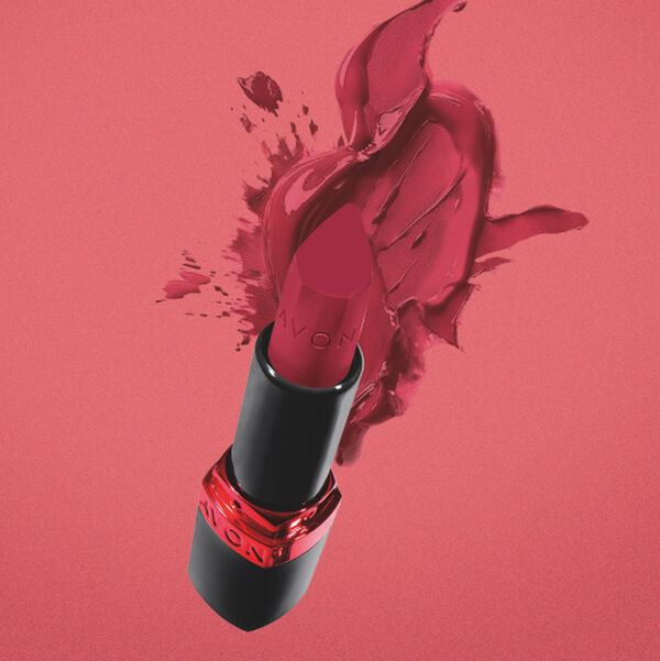 Batom em bala Avon aberto, na cor rosa-escura, posicionado em diagonal. Ao fundo, uma textura cremosa e espessa do mesmo produto está espalhada em formato de pincelada sobre uma superfície rosa.