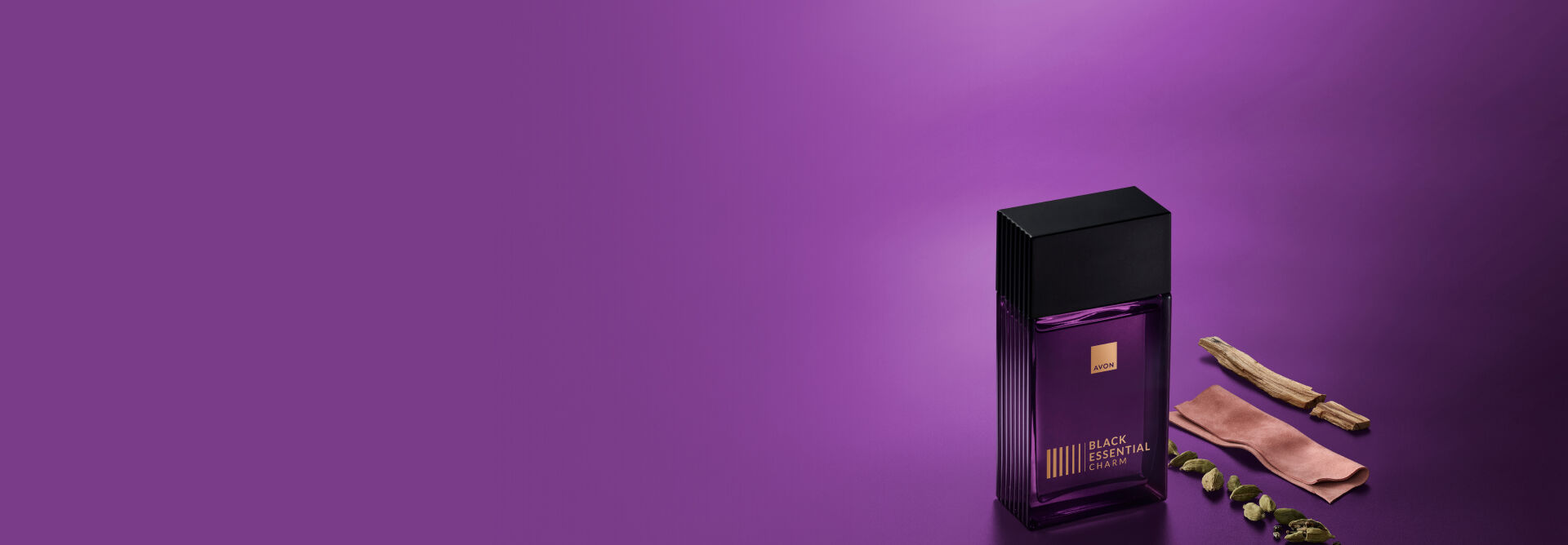 Black Essential Charm, com frasco de vidro retangular violeta, letras douradas e tampa preta, aparece ao lado de amostras de cardamomo, couro e sândalo, ingredientes da fragrância. Fundo violeta.
