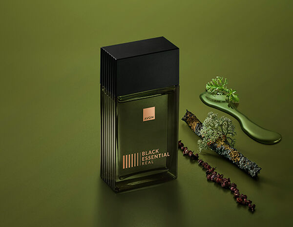 Fragrância Black Essential Real com ingredientes como pimentas e plantas, em fundo verde.