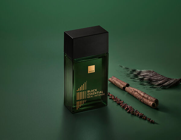 Fragrância Black Essential Real com ingredientes como pimentas e plantas, em fundo verde.