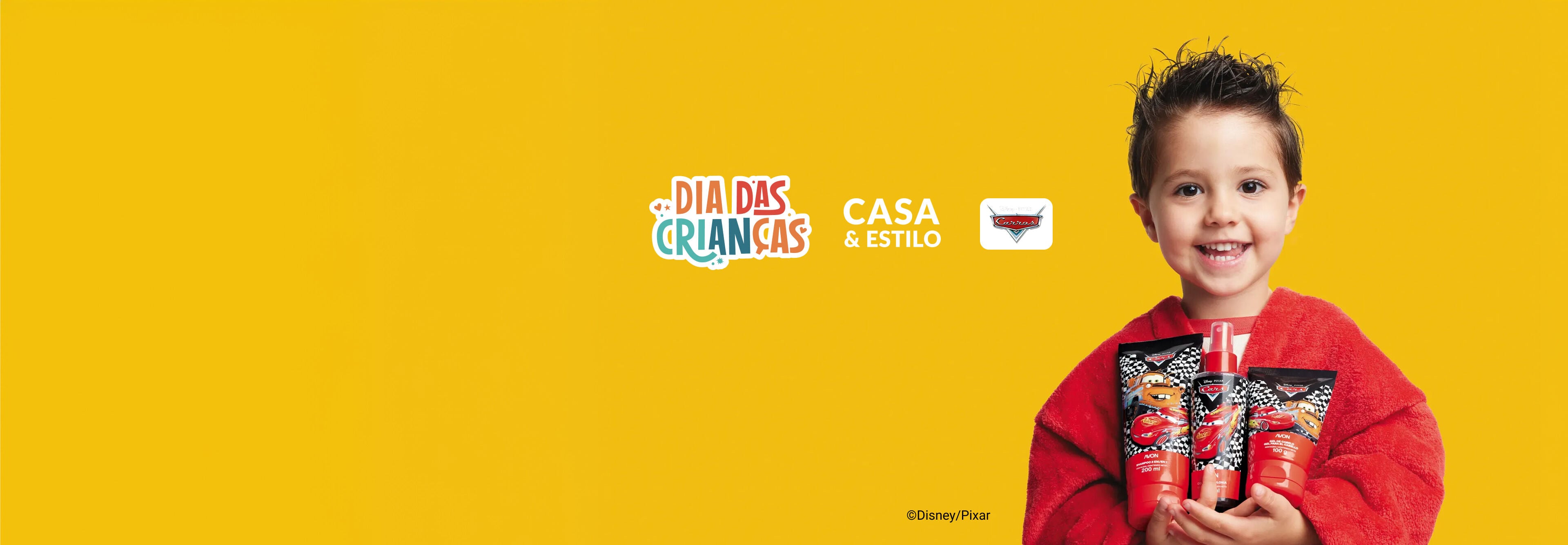 Menino sorridente de roupão vermelho segura três produtos da linha Carros. Ao fundo amarelo, destacam-se os logos Dia das Crianças, Casa & Estilo e Carros.