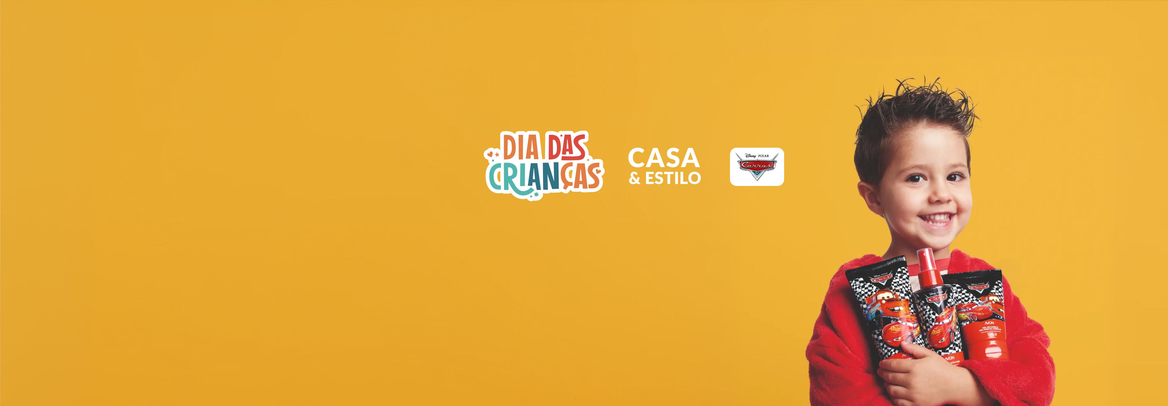 Menino sorridente de roupão vermelho segura três produtos da linha Carros. Ao fundo amarelo, destacam-se os logos Dia das Crianças, Casa & Estilo e Carros.