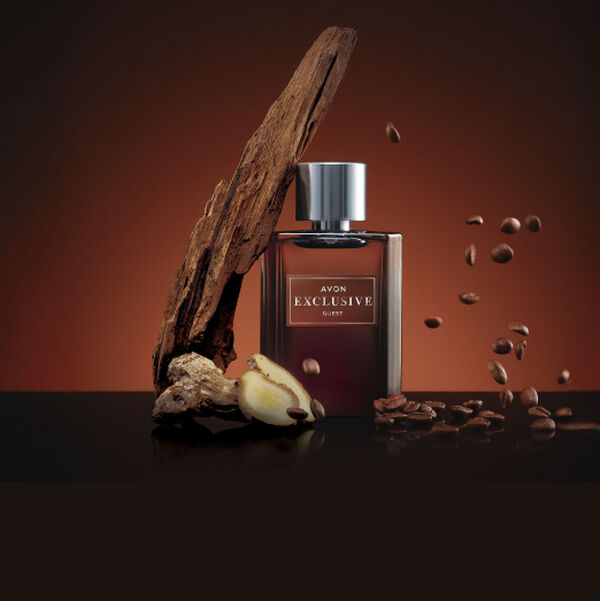 Frasco marrom com tampa prata da fragrância Exclusive Guest, cercado de ingredientes como madeira, gengibre e grãos de café, sobre bancada marrom-escuro, em fundo marrom.