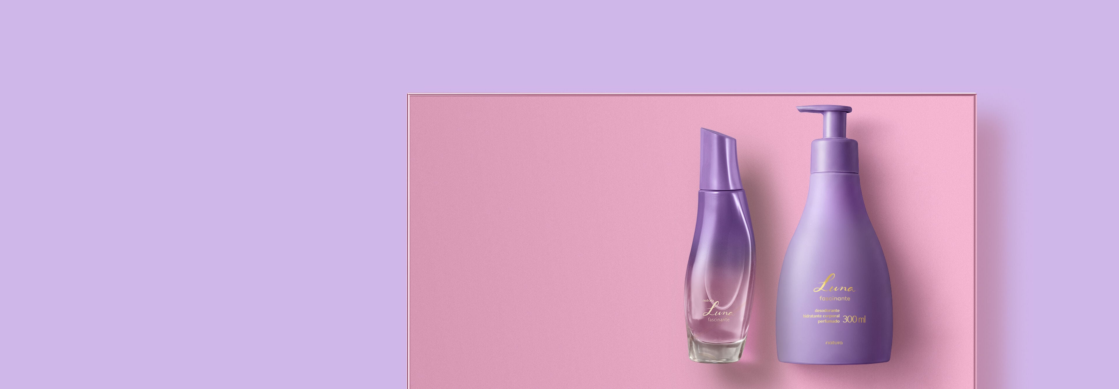 Perfume e hidratante corporal Natura Luna Fascinante roxos posicionados sobre base rosa. A embalagem de vidro curvilínea e o frasco com válvula dosadora destacam o tom lilás do fundo.