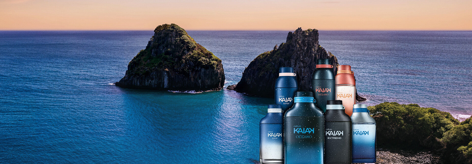 Frascos de fragrâncias Kaiak sobre a água azul do mar, com ilhas rochosas e céu em tons de azul e laranja ao fundo.