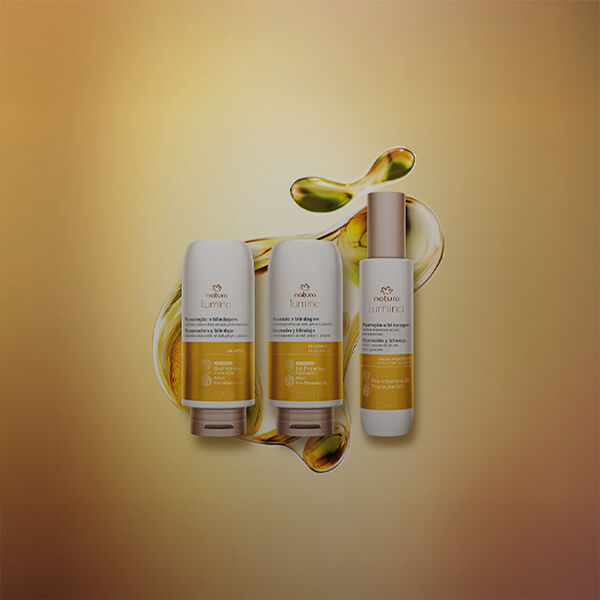 Produtos da linha Lumina Restauração e Blindagem: Shampoo, Máscara e Spray Protetor UV, em fundo amarelo com grafismo branco e dourado semitransparente. Embalagens brancas e com detalhes amarelo.