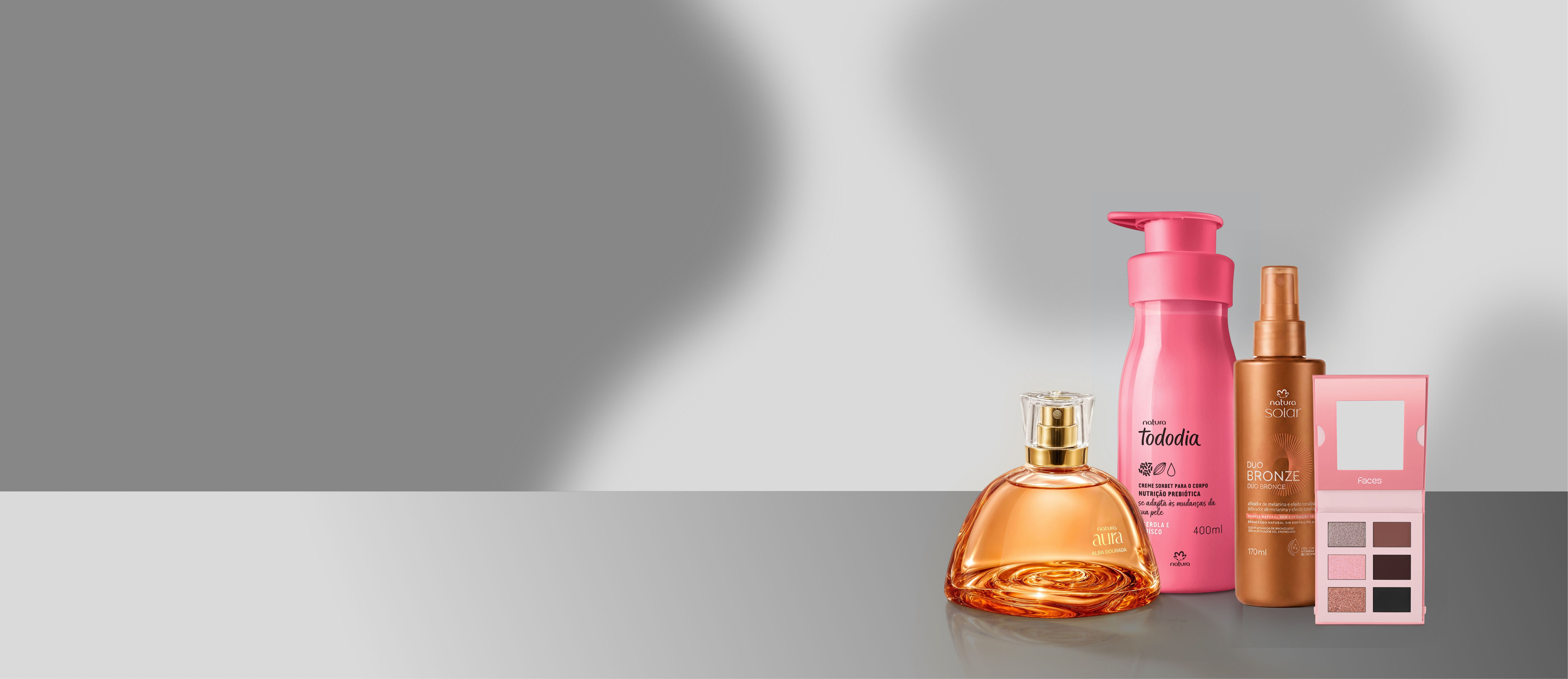 Os produtos Aura Alba Dourada, Tododia Hidratante Acerola e Hibisto, Sérum ativador de bronzeado e paleta de sombras Faces, aopoiados em um ums locsl lido cinza e com fundo cinza