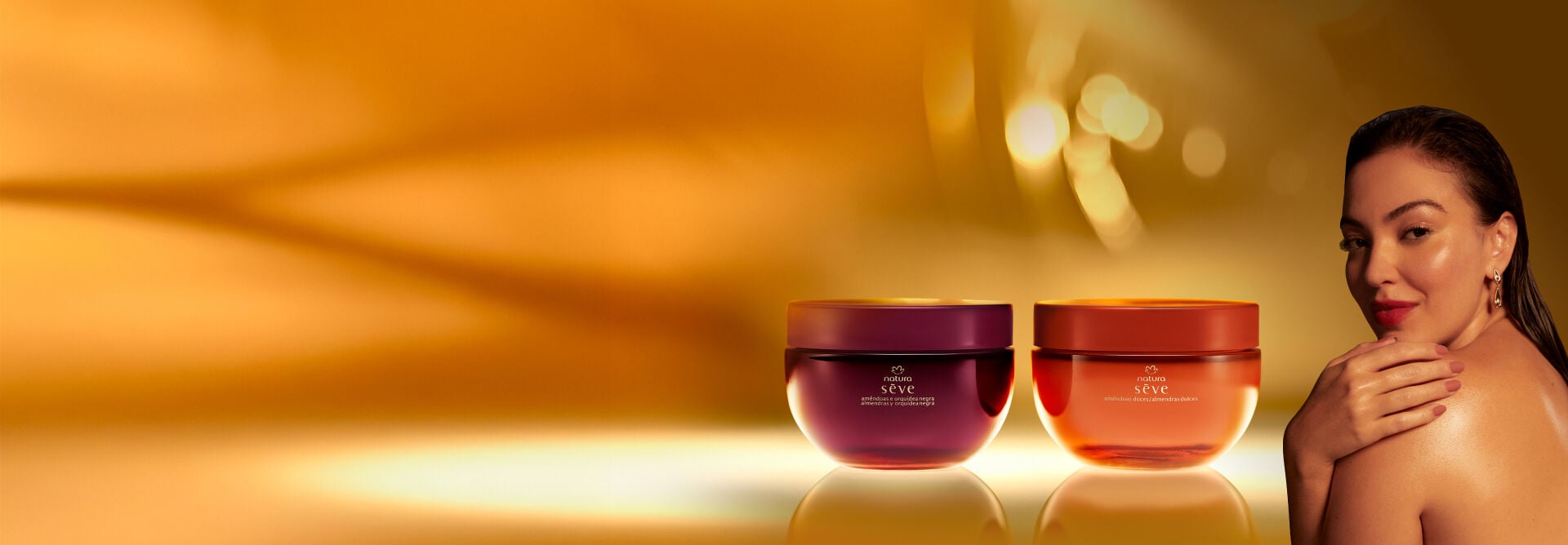 Natura Sève Creme Desodorante Corporal Perfumado Amêndoas e Orquídea Negra, em tom de roxo, e Amêndoas Doces, em tom de laranja, destacam-se em superfície e fundo iluminados em tom de dourado.