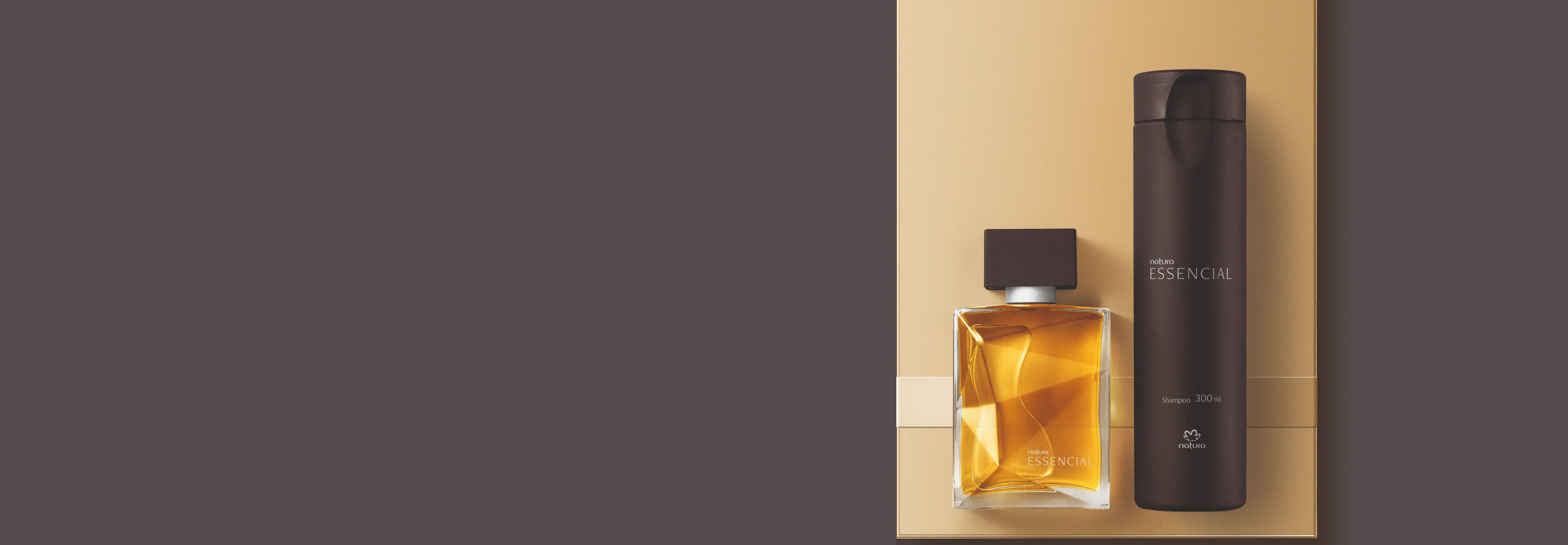 Frasco de perfume Natura Essencial em vidro lapidado dourado e frasco de shampoo marrom cilíndrico alinhados sobre base bege. O cenário em tons sóbrios reforça a sofisticação das embalagens.
