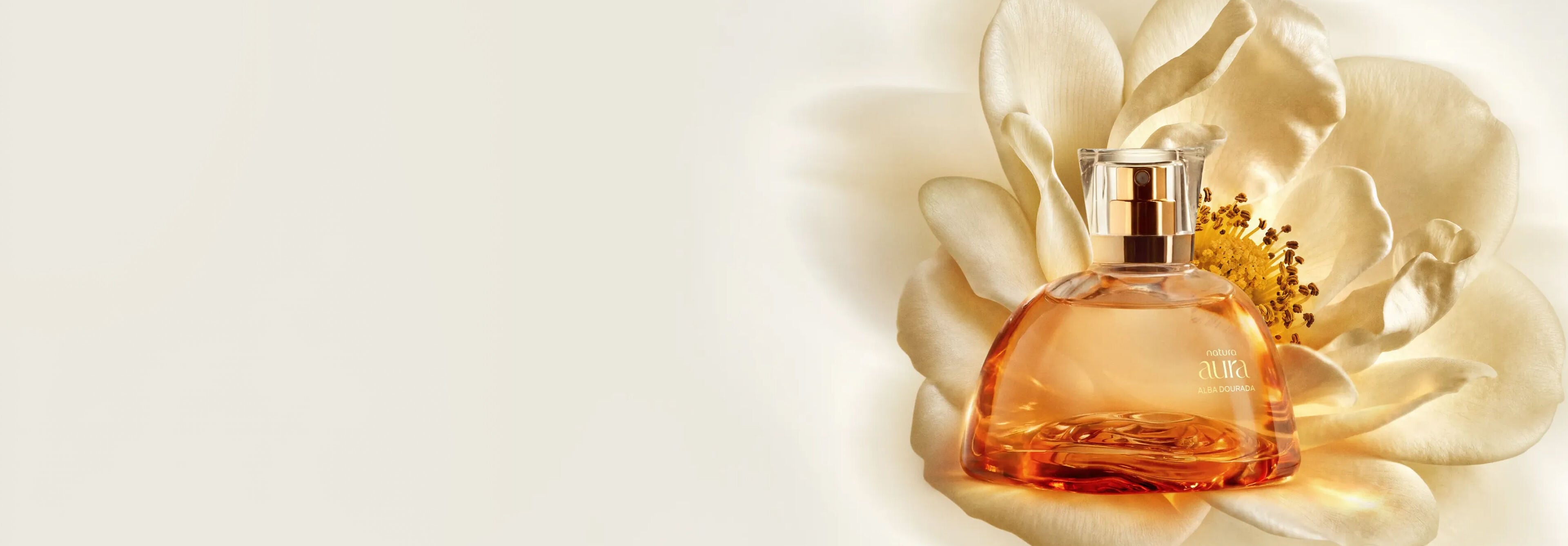 Imagem do novo Eau de Parfum Natura Aura Alba Dourada, um frasco translúcido luxuoso com líquido dourado, com uma Flor de Mel ao fundo.