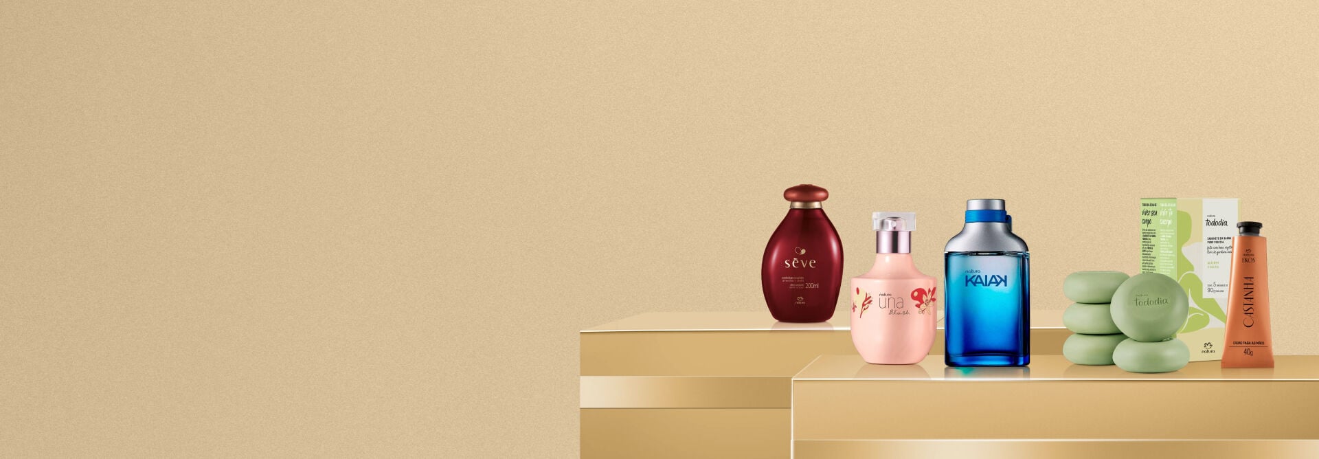 Produtos de diferentes linhas da Natura, incluindo Sève, Una Blush, Kaiak, Ekos Castanha e Tododia Alecrim e Sálvia dispostos sobre caixas de presente douradas.