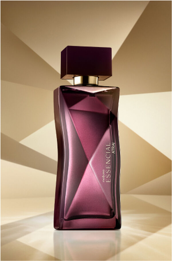 Frasco de Essencial Atrai Feminino, em tons de roxo, aparece em destaque no centro da tela sobre fundo multifacetado dourado, fazendo alusão ao design do frasco de Essencial.