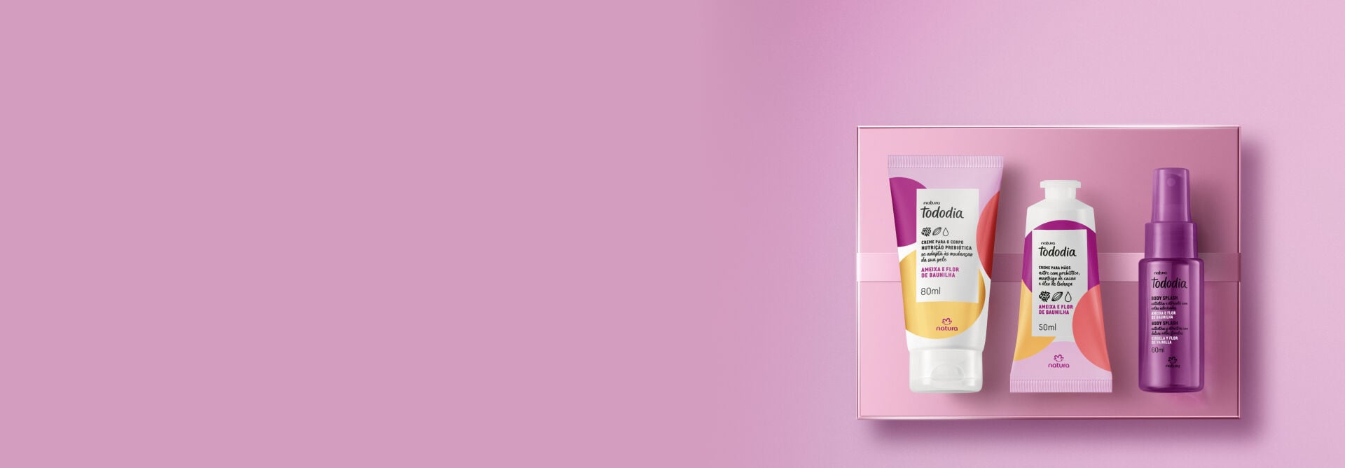 Presente Natura Tododia Feliz Aniversário, incluindo 1 body splash, 1 creme para o corpo e 1 creme para as mãos Ameixa e Flor de Baunilha, sobre caixa de presente acetinada lilás. Fundo lilás.