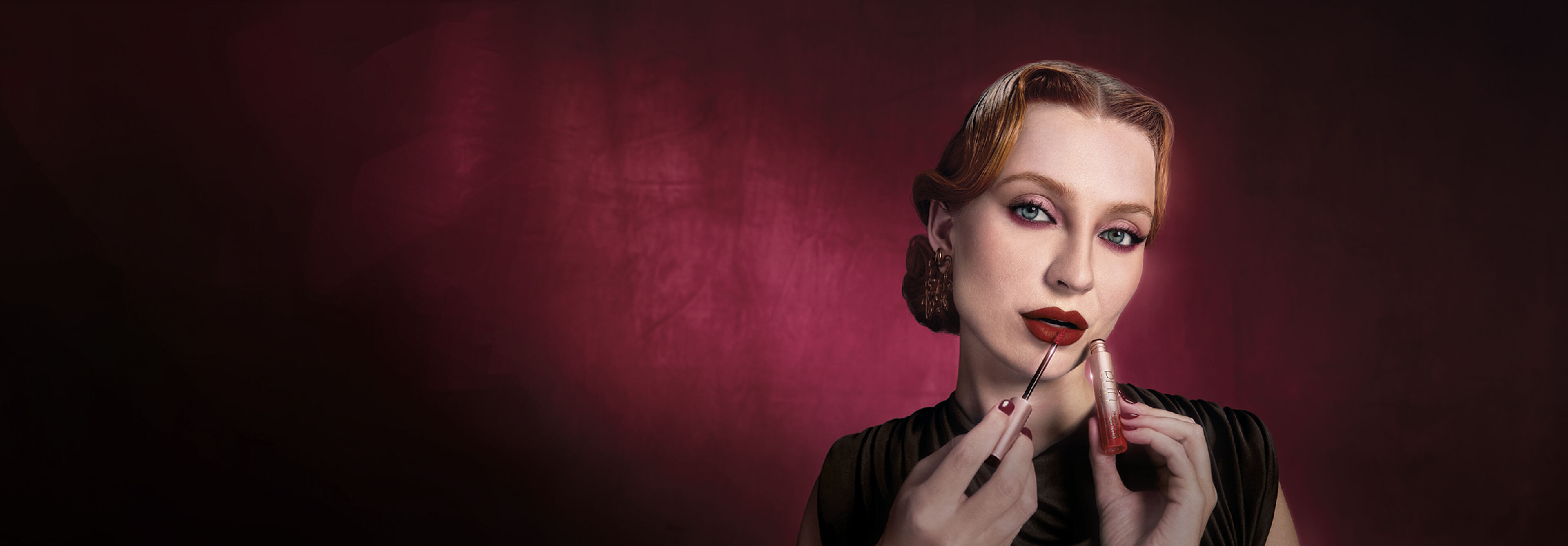 Foto de mulher, branca, ruiva, vestindo preto e usando uma maquiagem no estilo gótico com tons de vermelho. Posa aplicando nos lábios o Batom Líquido Matte Intransferível Una Vermelho-1.