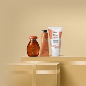 Presente Natura Queridinhos, com 1 Óleo Corporal Sève Amêndoas Doces, 1 Polpa para as Mãos Ekos Castanha e 1 Creme Nutritivo para o Corpo Tododia Macadâmia sobre caixas de presentes em fundo bege.