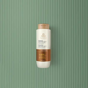 Pote creme com tampa e rótulo dourados de Máscara Antissinais Natura Lumina. Fundo em verde com listras verticais.