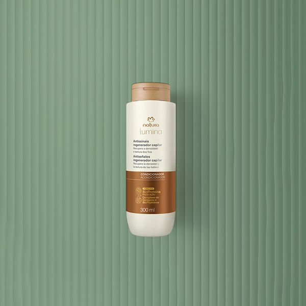 Pote creme com tampa e rótulo dourados de Máscara Antissinais Natura Lumina. Fundo em verde com listras verticais.