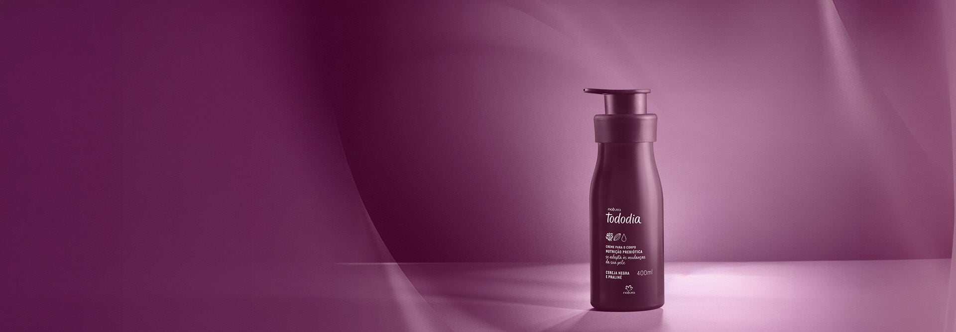 Frasco roxo-escuro com tampa pump do Creme Desodorante Nutritivo Tododia Cereja Negra e Praliné em fundo roxo iluminado.