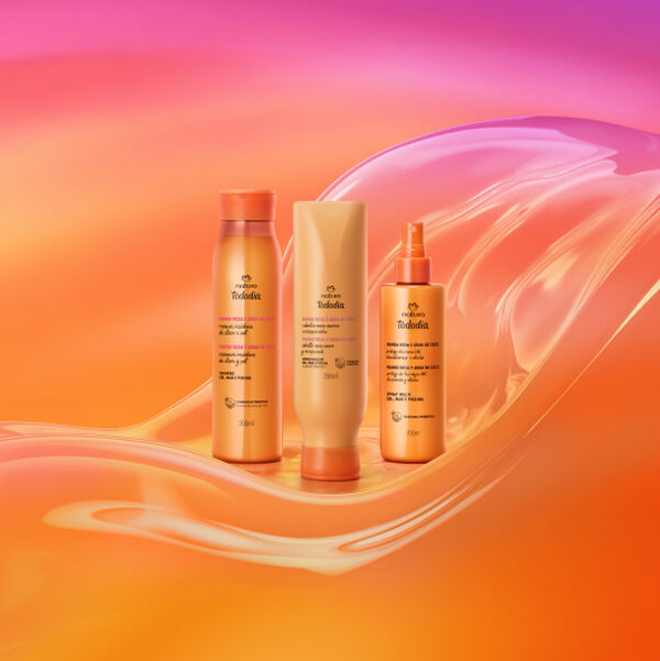 Três produtos Natura Tododia Manga Rosa e Água de Coco para cabelos. Um shampoo, um condicionador e um spray em embalagens alaranjadas brilhantes, dispostos sobre fundo ondulado laranja e rosa.