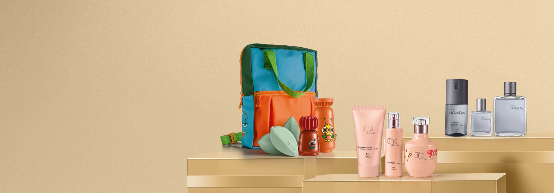 Kits Natura dispostos sobre pedestais dourados em fundo bege. À esquerda, mochila e itens infantis Naturé; ao centro, produtos Una Blush em tom rosa-nude; à direita, itens masculinos Natura Homem.