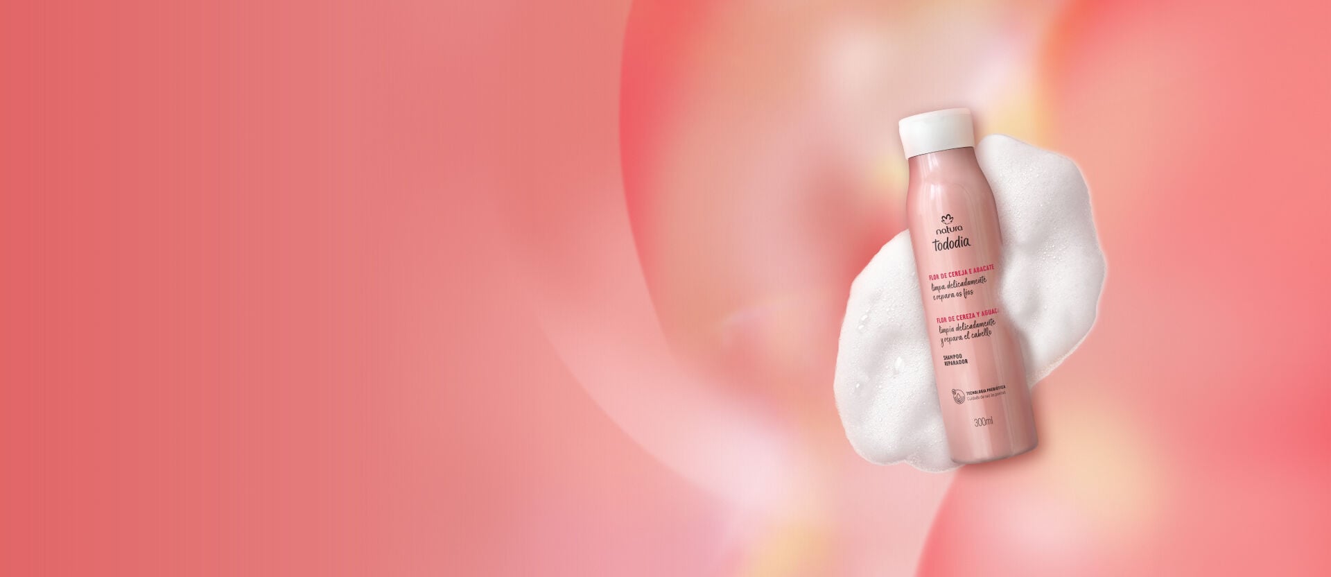 Shampoo Reparador Flor de Cereja e Abacate com textura de espumas ao redor do frasco sobre fundo rosa.