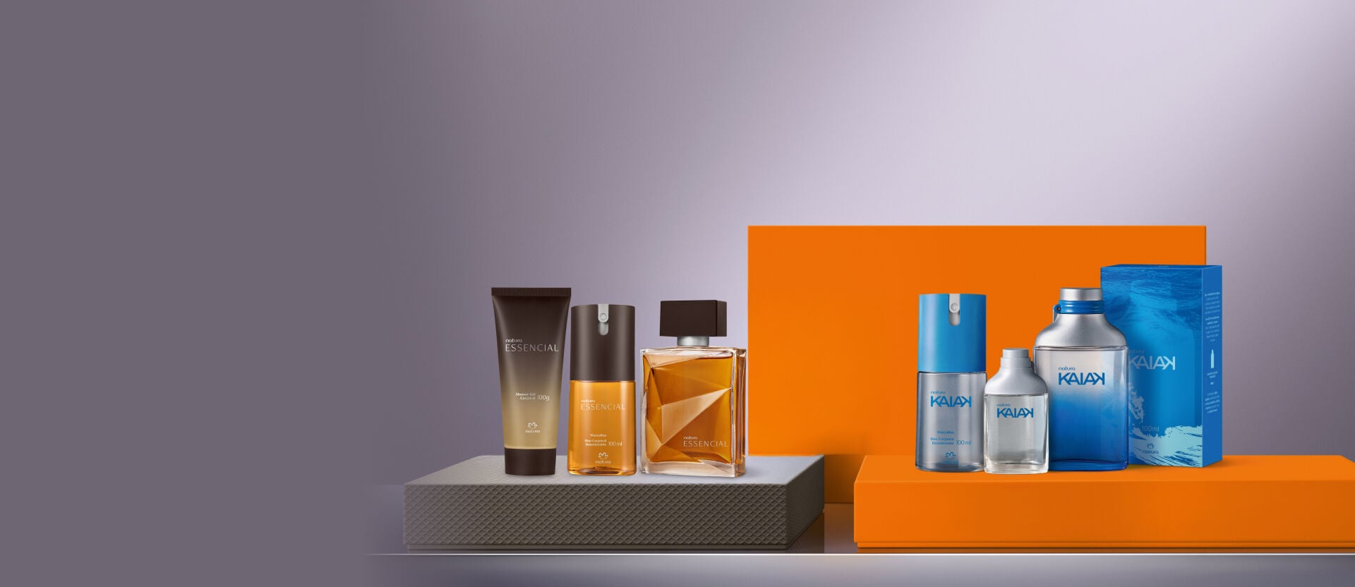 Duas linhas de perfumes masculinos Natura dispostas lado a lado: à esquerda, o kit Essencial com shower gel, desodorante e colônia; à direita, sobre uma base laranja, a linha Kaiak com desodorante, miniatura, colônia e caixa azul.