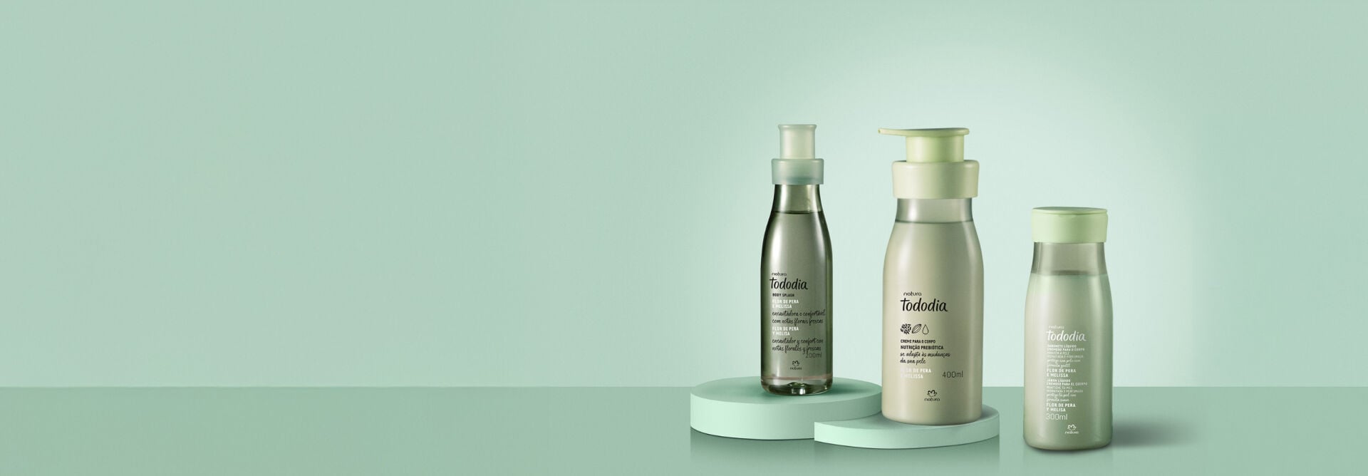 Itens Tododia Flor de Pera e Melissa: Body Splash, Creme para o Corpo e Sabonete Líquido sobre superfície verde, em fundo verde-claro.