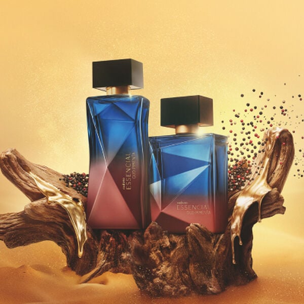 Dois frascos de perfume Natura Essencial Oud Pimenta, um masculino e um feminino, em tons de azul e bordô, sobre uma base de madeira com grãos de pimenta ao lado.