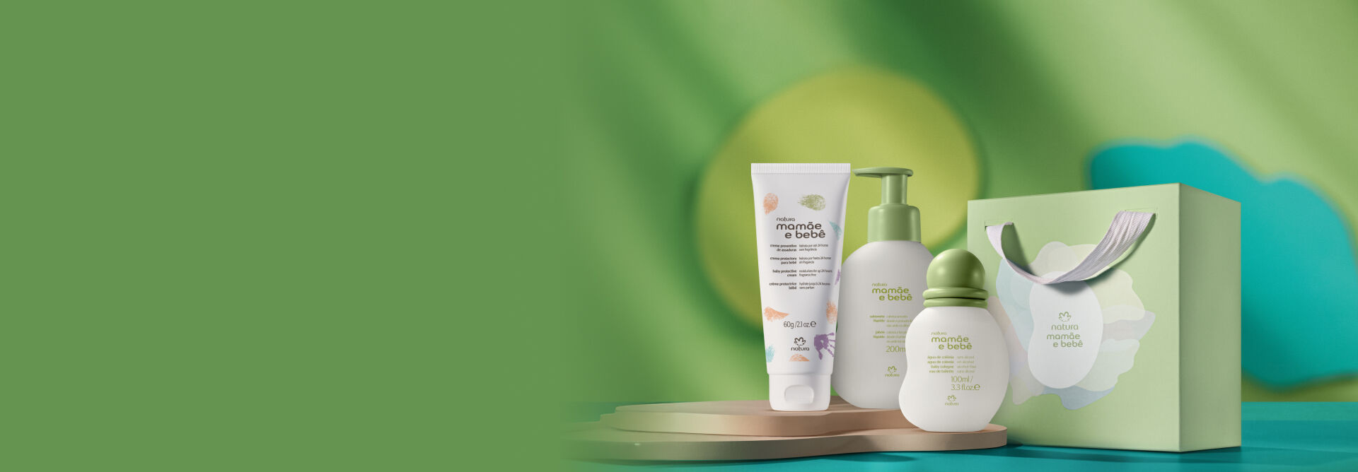 Presente Mamãe e Bebê, incluindo 1 água de colônia, 1 sabonete líquido, 1 creme preventivo de assaduras e 1 sacola de presente em fundo verde-claro com formas orgânicas azuis e amarelas.
