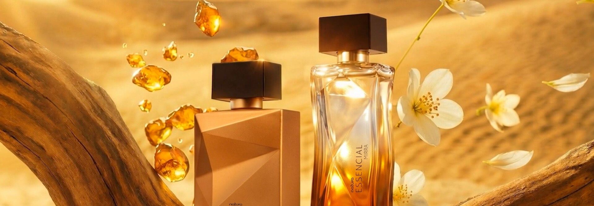 Vídeo com cristais âmbar caindo sobre deserto e sobre frascos de fragrâncias masculina e feminina de Essencial Mirra. Flores brancas caem sobre frasco feminino, com destaque para os detalhes dos vidros facetados. Destaque final para frascos sobre tronco em madeira, com flores brancas e âmbar. Fundo amarelo-claro.