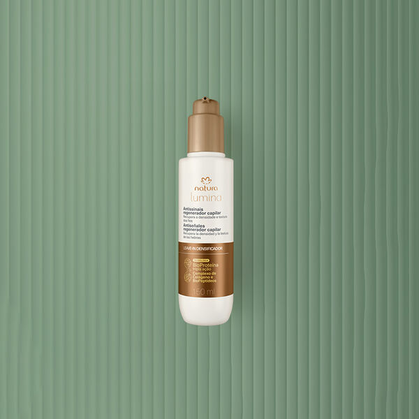Frasco creme com válvula e rótulo dourados de Sérum de Prevenção Antissinais Natura Lumina. Fundo em verde com listras verticais.