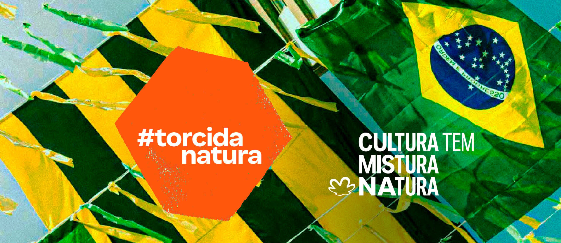 Fundo de céu azul com uma bandeira do Brasil e fitinhas verdes e amarelas. Hexágono laranja com o texto: tem Brasil na rua. Texto aplicado ao fundo: tem cultura mistura Natura.