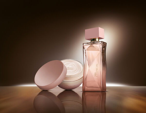 Na cena, Desodorante Hidratante Corporal Perfumado Essencial Feminino e Deo Parfum Essencial Feminino aparecem iluminados sobre superfície marrom em fundo escuro.
