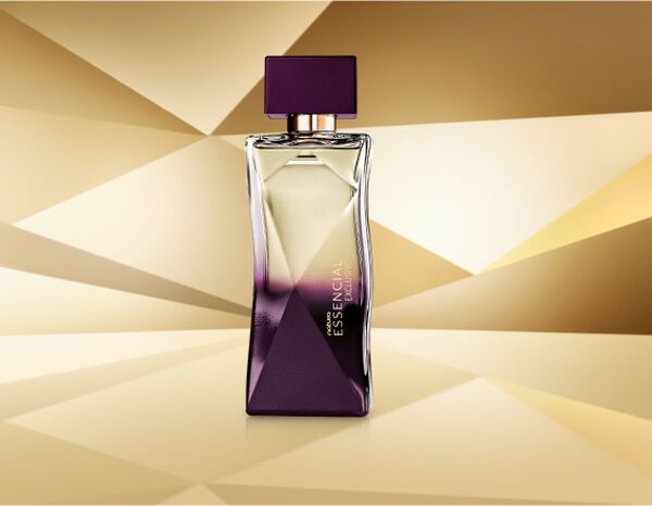 Frasco de Essencial Exclusivo Feminino, com topo transparente e base roxa, aparece em destaque no centro da tela sobre fundo multifacetado dourado, fazendo alusão ao design do frasco de Essencial.