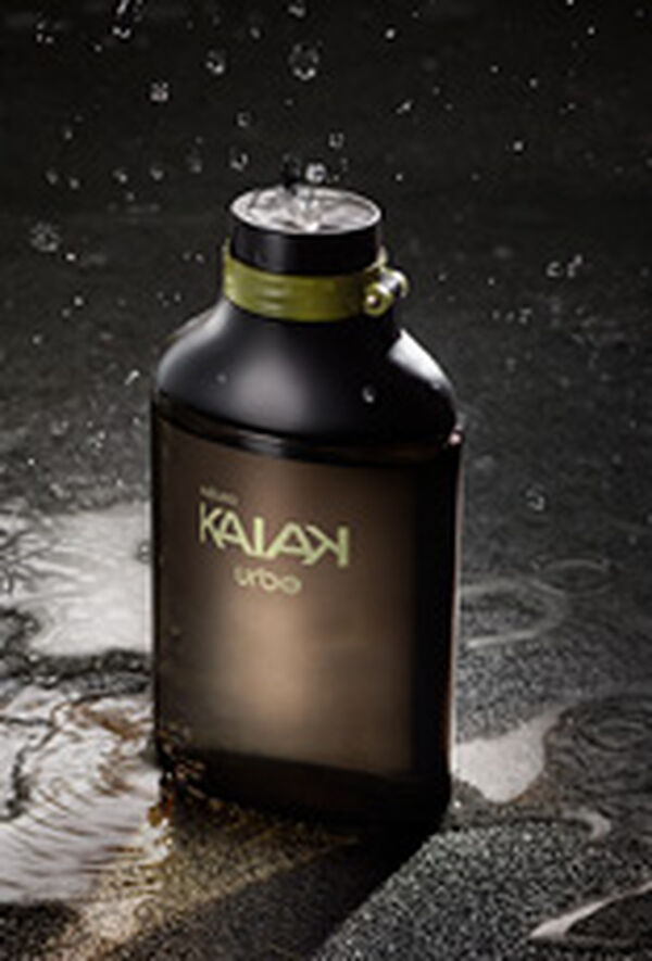 Frasco preto e verde fosco de fragrância Desodorante Colônia Kaiak Urbe sobre superfície molhada com respingos e gotas em fundo escuro.