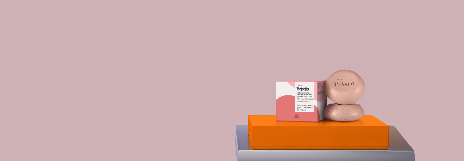 Fundo rosa-antigo destaca Kit Sabonete em Barra Natura Tododia Tâmara e Canela sobre caixa laranja.