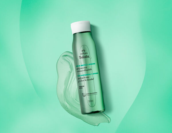 Frasco verde translúcido com tampa branca do Shampoo Detox Tododia Chá de Hortelã e Gengibre. Está sobre um rastro de gel verde em fundo degradê verde.