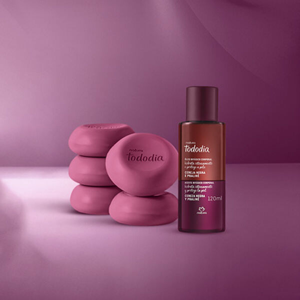 Linha Tododia Cereja Negra e Praliné com 5 sabonetes redondos, 1 frasco de body splash, 1 pump de creme, 1 pote de creme veludo e 1 frasco de óleo corporal. Embalagens roxas em fundo roxo iluminado.