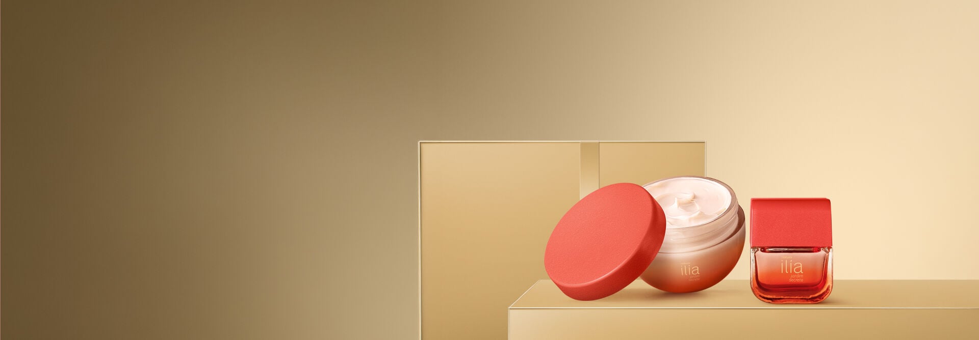 Pote de creme corporal Natura Ilía Jardim Secreto aberto mostrando textura cremosa com tampa vermelha apoiada. Ao lado, o embalagem da fragrância em tom degradê avermelhado sobre base dourada. 