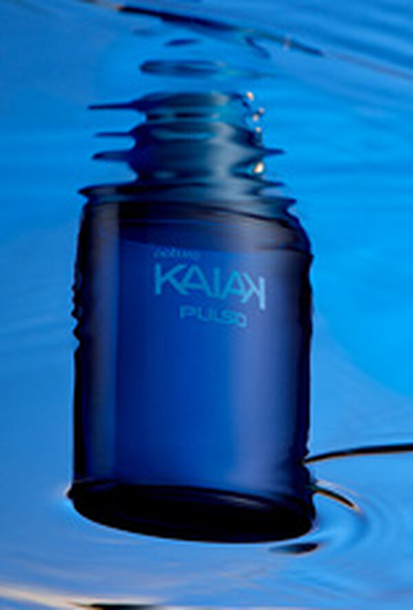 Frasco azul-escuro da fragrância Kaiak Pulso flutuando em água azul, com reflexos ondulados.