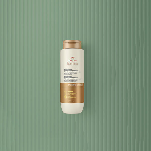 Embalagem creme com tampa e rótulo dourados de Condicionador Antissinais Natura Lumina. Fundo em verde com listras verticais.