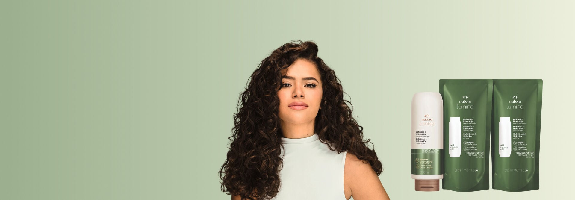 A atriz Maisa Silva, sorrindo e com cabelos cacheados volumosos, posa à esquerda. À direita, um frasco e dois refis do creme de pentear Natura Lumina Definição e Hidratação. O fundo é verde-claro.