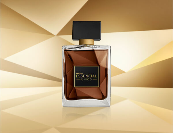 Frasco de Essencial Único Masculino, em vidro translúcido com fragrância em tons de âmbar e tampa preta, aparece iluminado sobre superfície e fundo dourados.
