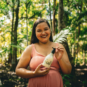 Foto de mulher, em uma floresta tropical, segurando uma Loção Corporal Natura Ekos Andiroba.