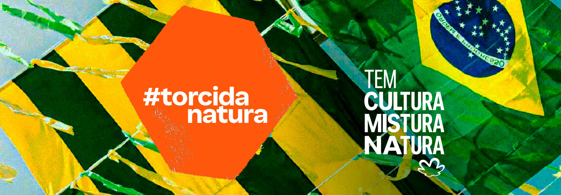 Fundo de céu azul com uma bandeira do Brasil e fitinhas verdes e amarelas. Hexágono laranja com o texto: tem Brasil na rua. Texto aplicado ao fundo: tem cultura mistura Natura.