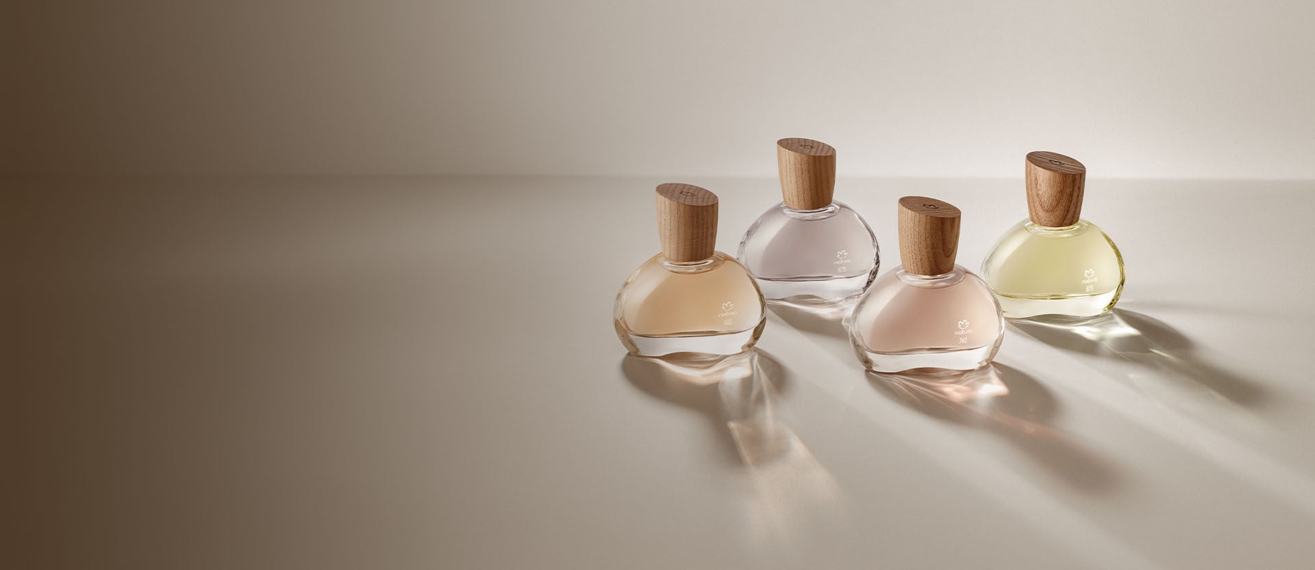 Quatro frascos de perfume com tampas de madeira, em diferentes tonalidades, dispostos em um fundo neutro.